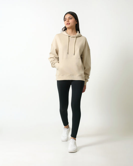 Person wearing a beige hoodie, black leggings, and white sneakers on a white background